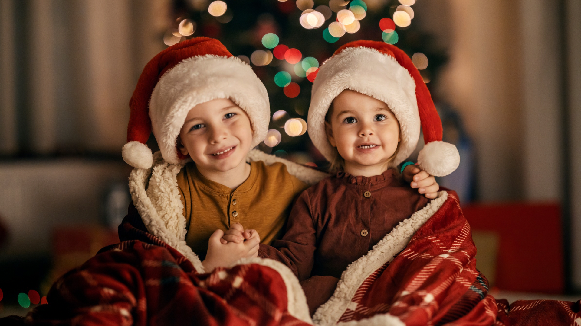 Portrait of a cheerful brother and sister sitting at home on christmas and new year's eve, embracing and smiling at the camera.